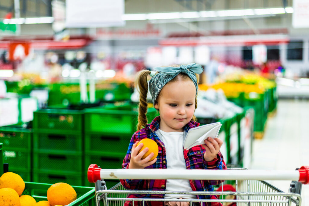 Petite fille sur un chariot dans un supermarché qui vérifie la liste de course